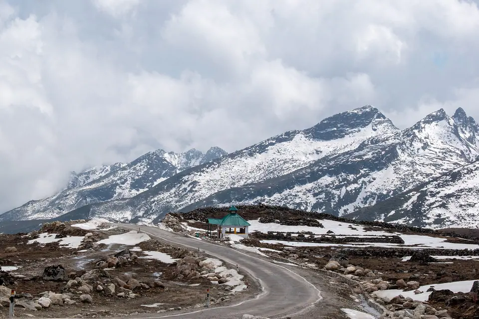 A road winding across a snow-dusted plateau below sharp peaks on the way to Bum La