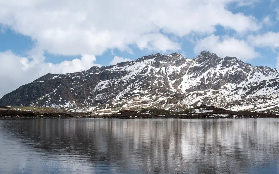 Snow-streaked mountains reflected in still Shree Swayambhu Lake near Bum La Pass