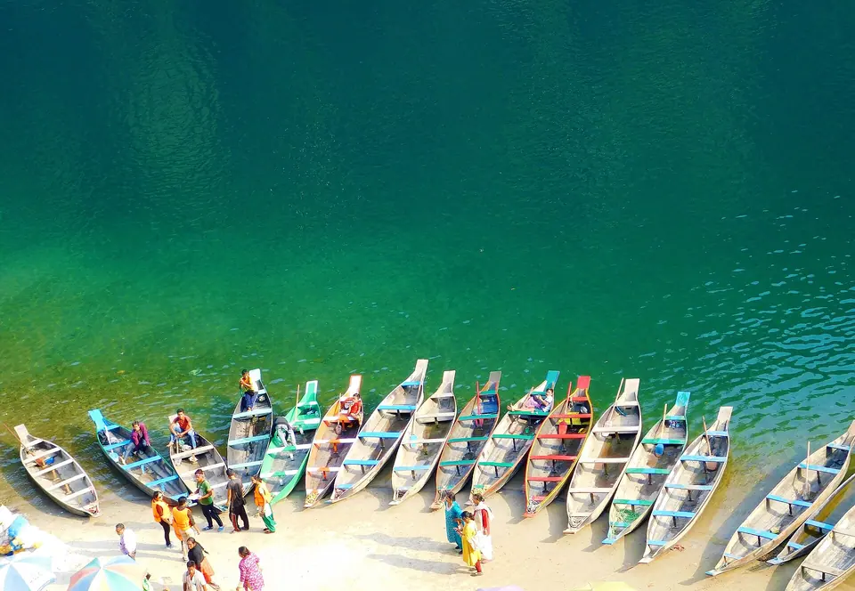 Rows of painted wooden boats pulled up on a sandbar beside the emerald Umngot River, Dawki