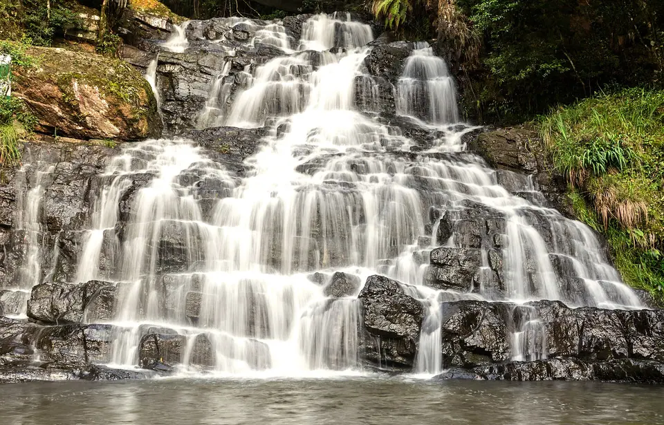 Water cascading over stepped dark rock at Elephant Falls near Shillong, framed by ferns and moss