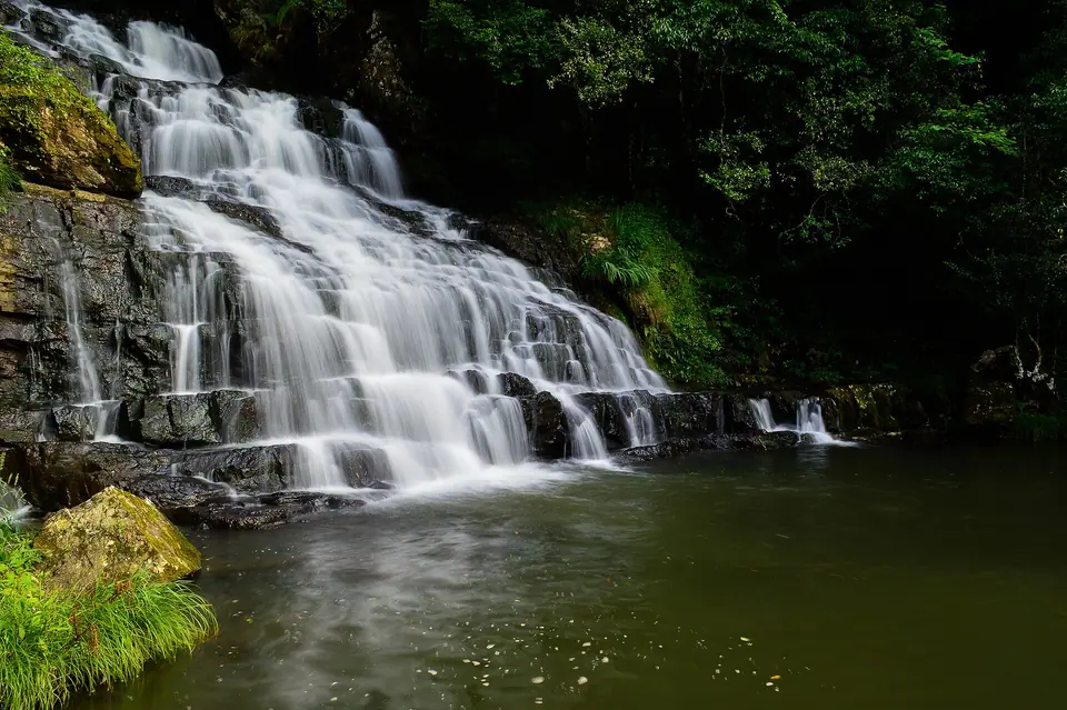 Long exposure of Elephant Falls spreading over rock steps into a calm green pool, Shillong