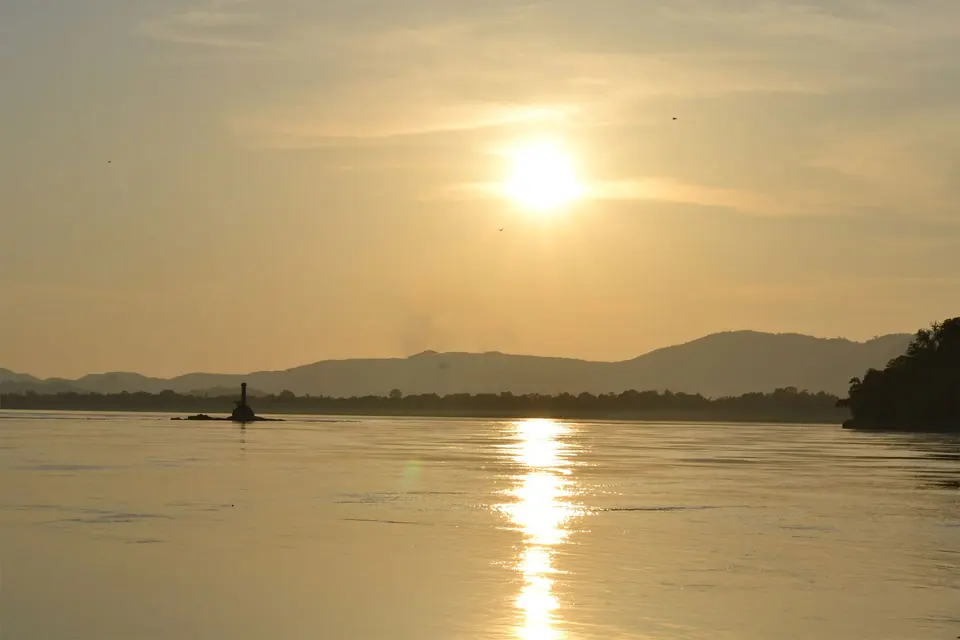 The sun setting over the Brahmaputra at Guwahati, with low hills and a boat on the golden water