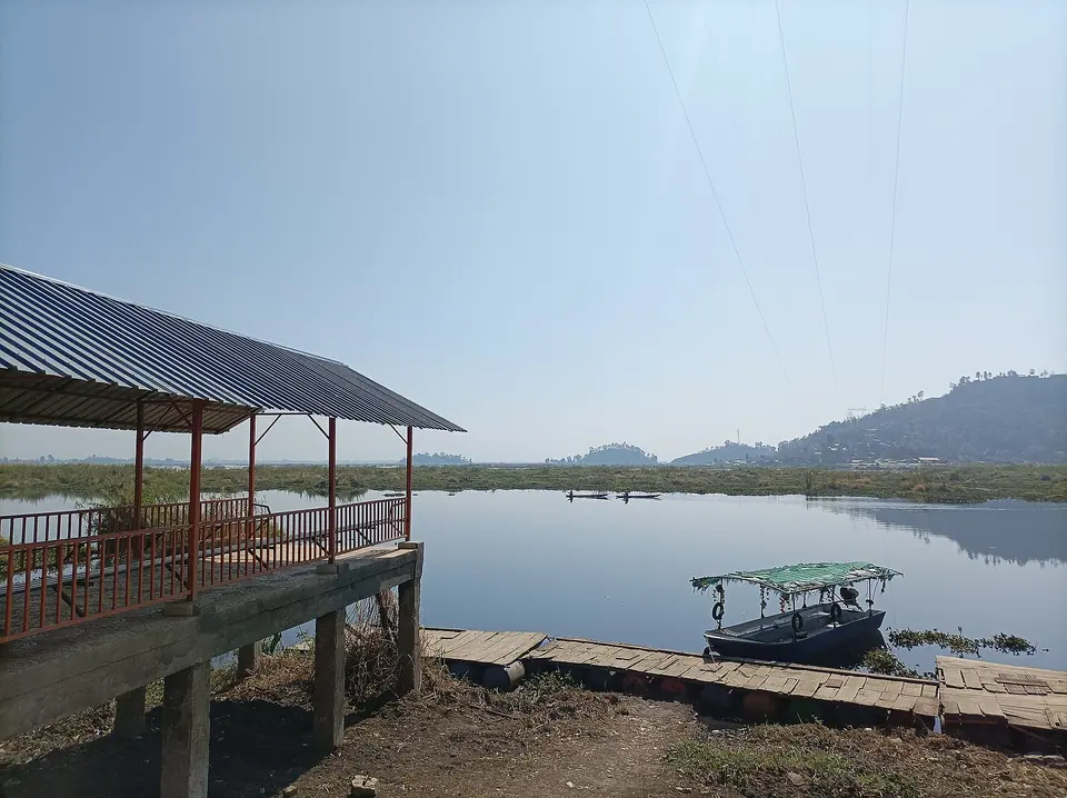 A jetty and small boats on the calm water of Loktak Lake, with low hills beyond