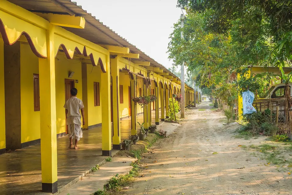 Yellow-painted colonnade of the Auniati Satra monastery on Majuli, with a sandy lane alongside