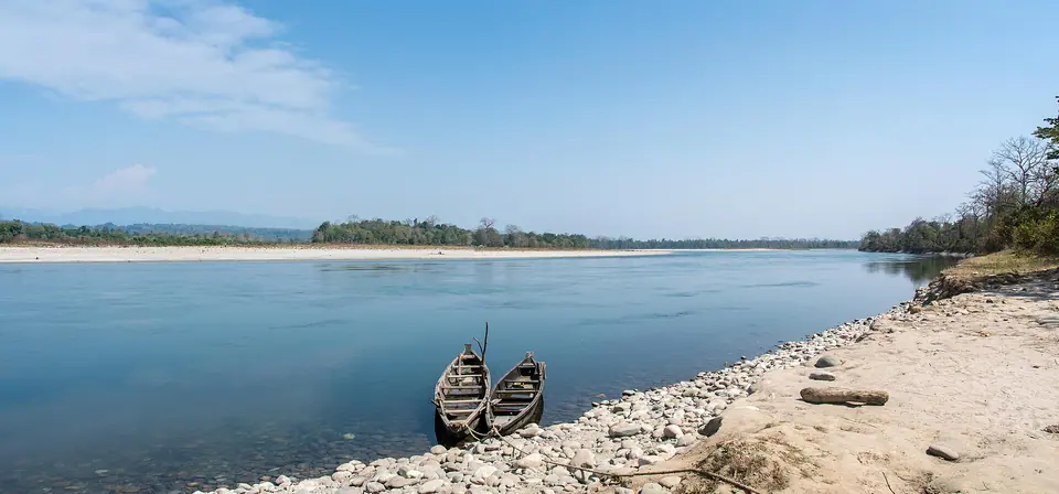 Two wooden boats on the pebble shore of the wide, blue Jia Bhoroli river at Nameri