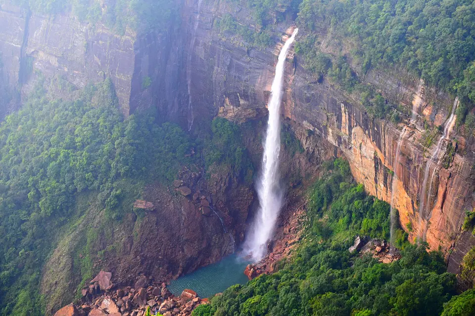 Nohkalikai Falls plunging 340 m down a sheer red-brown cliff into a green pool, Sohra