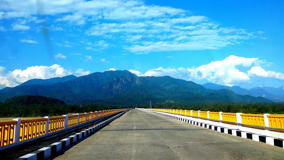A long yellow-railed road bridge leading toward the hills around Pasighat under a blue sky