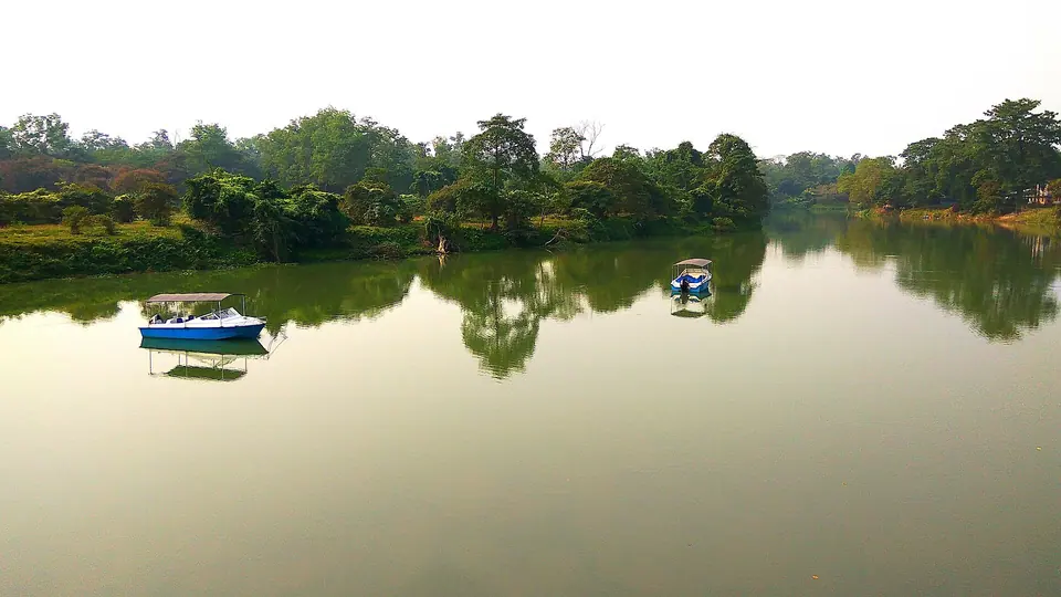 Small boats on a still, tree-lined lake inside Pobitora Wildlife Sanctuary near Guwahati