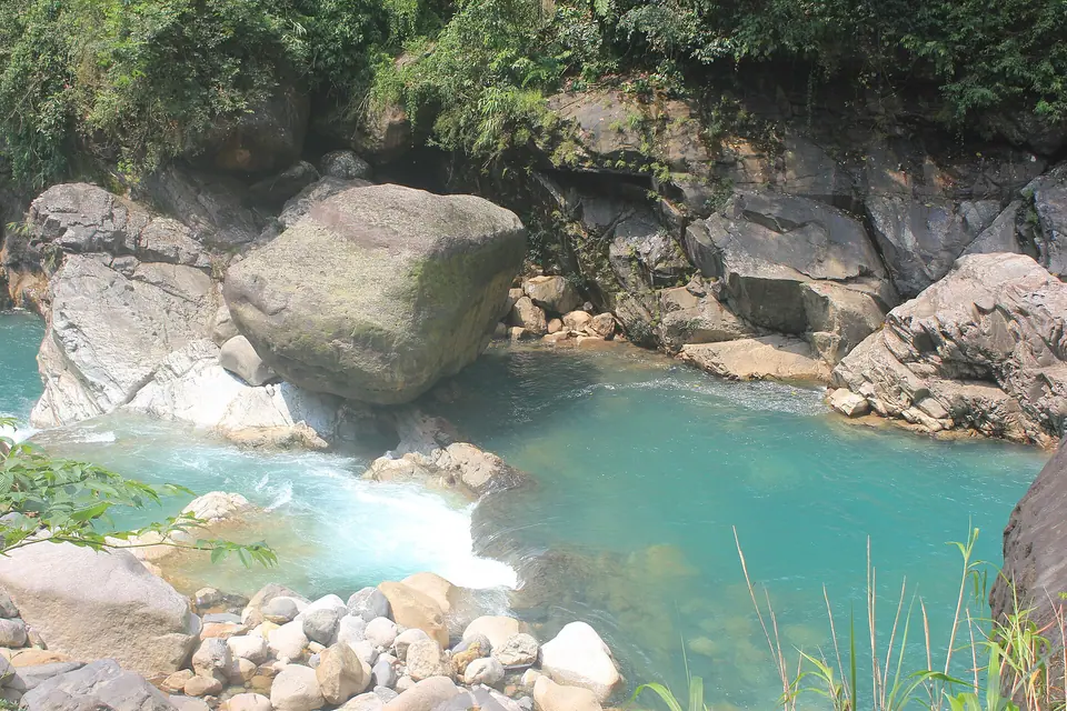 Turquoise stream flowing between large pale boulders in a forested gorge near Sohra