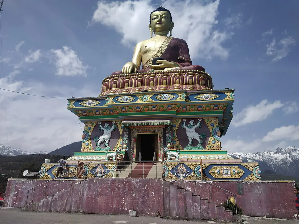 The giant seated Buddha statue on a painted plinth above Tawang, with snow peaks behind