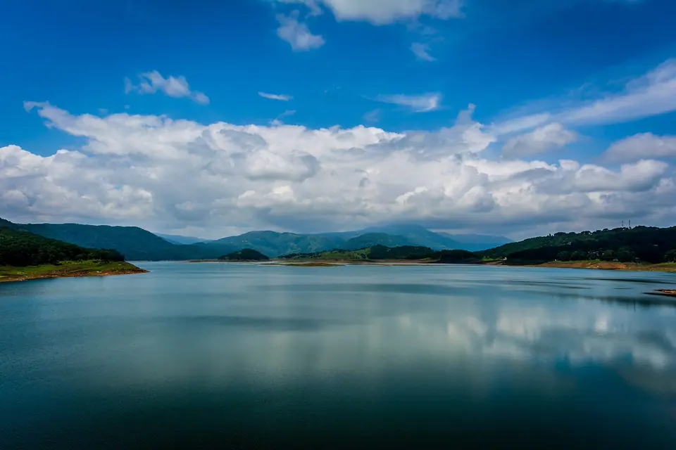 Still water of Umiam Lake reflecting clouds, with low green hills on the far shore