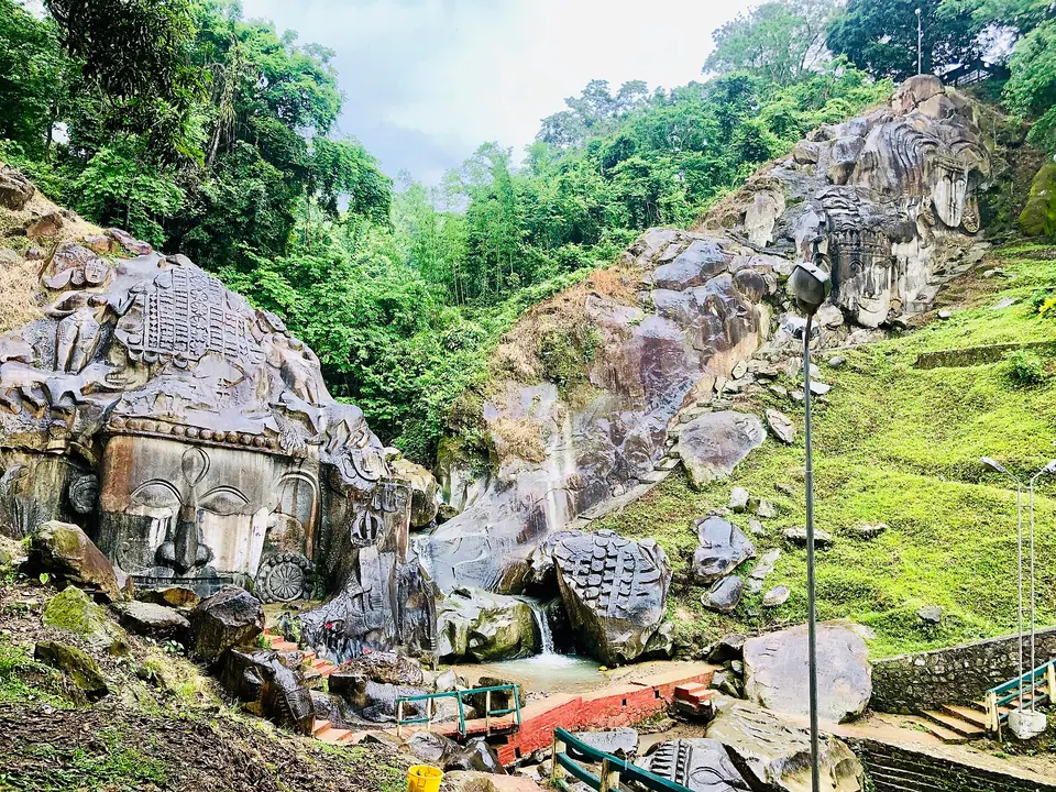 Carved rock faces and a small stream in the forested ravine at Unakoti