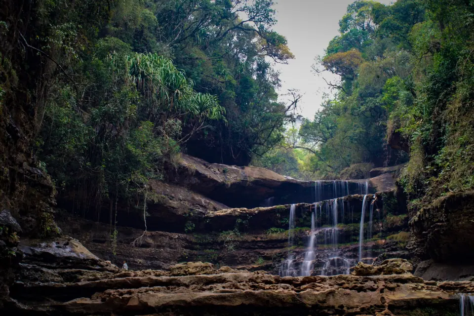 Thin cascades of Wei Sawdong falling over layered rock ledges under a forest canopy