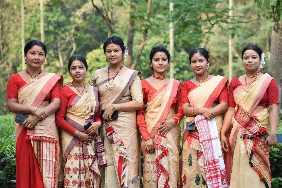 A group of Assamese women in red-bordered Bihu dress posing in a tea garden