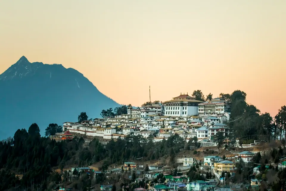 Tawang Monastery glowing on its ridge at dusk below a pointed blue mountain, Arunachal Pradesh