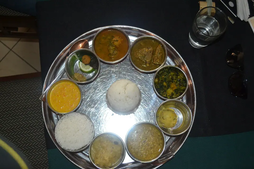 An Assamese thali with rice in the centre ringed by small bowls of dal, curries and greens