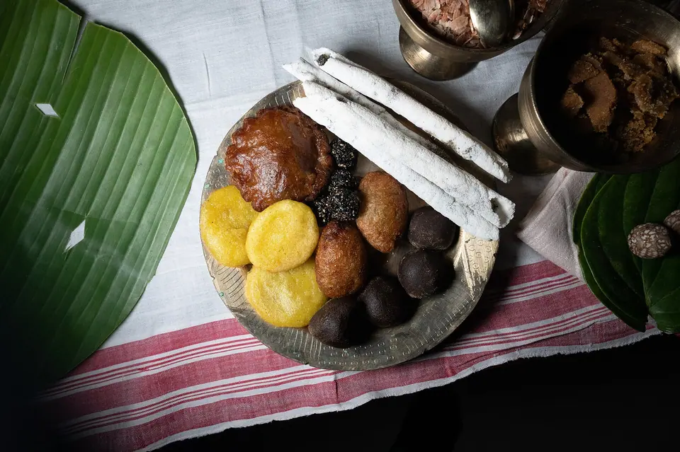 Assamese Bihu pitha rice cakes and laru sweets on a brass plate over a gamosa cloth