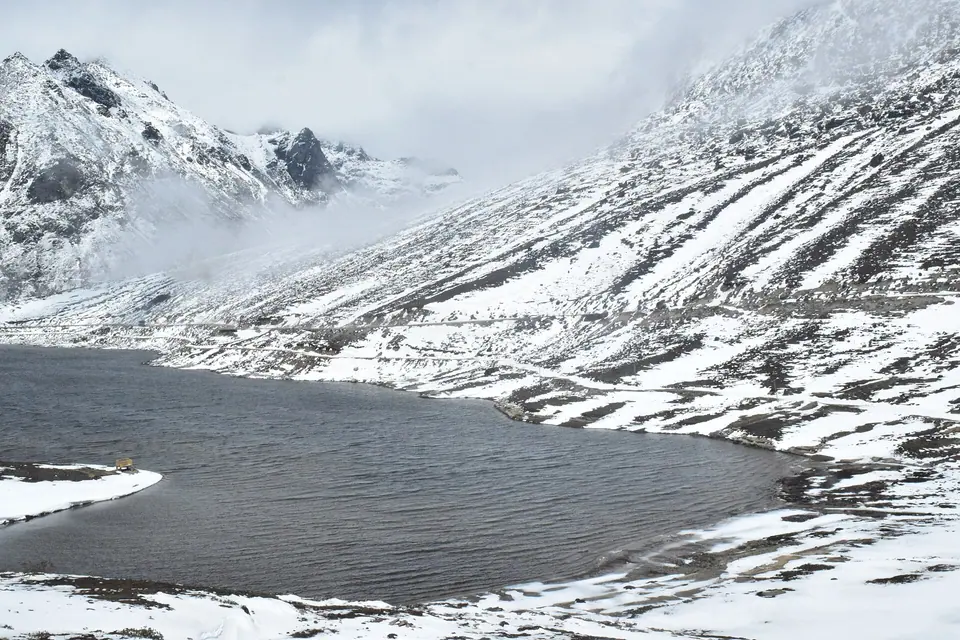 Snow-covered slopes wrapping around dark Sela Lake in winter, Sela Pass, Arunachal Pradesh